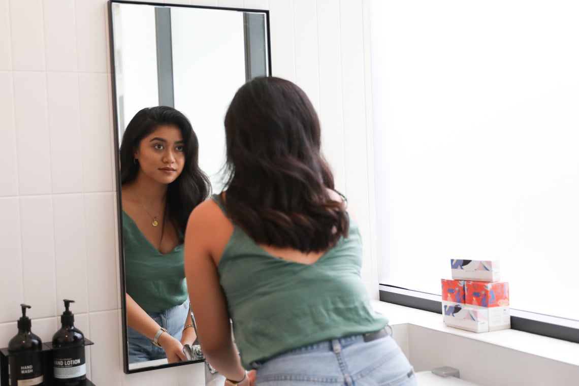 Woman looking at self in mirror in office toilet with free tampons